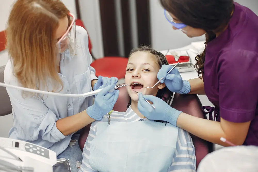 Child receiving dental cleaning from two hygienists
